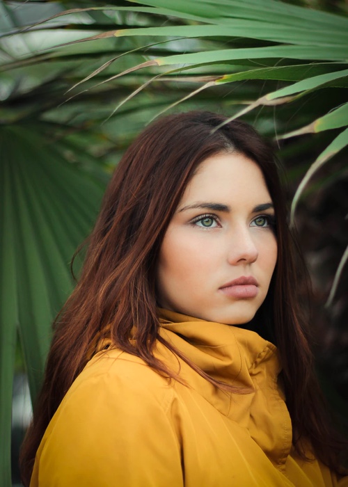 desinger, Willow, posed beside large green leaves in a yellow raincoat