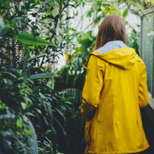 Designer, Willow, with her back turn away, facing folliage in a yellow raincoat